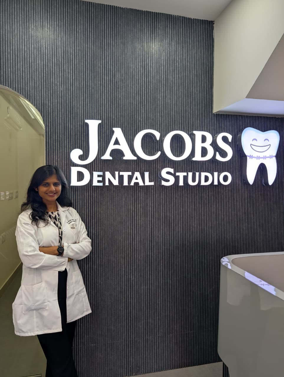Dr. Anju Sarah Jacob in reception, beside the lit JACOBS Dental Studio sign