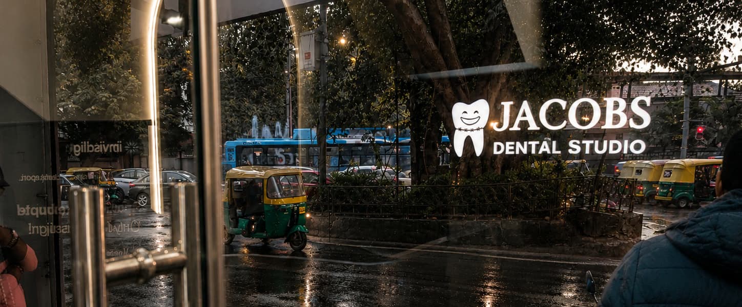 The JACOBS Dental Studio sign and Brigade Road at dusk, through the studio's glass front